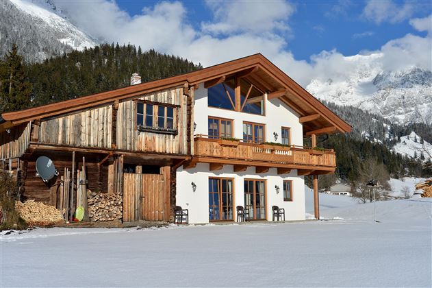 Ein charmantes Chalet in den Bergen, umgeben von Schnee. Die Fassade kombiniert Holz und weiße Wände, mit Blick auf die beeindruckenden Berge.