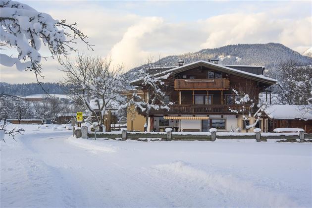 A cozy house in the snow, surrounded by a wintry landscape. The trees are covered in snow, and the atmosphere is calm and peaceful.