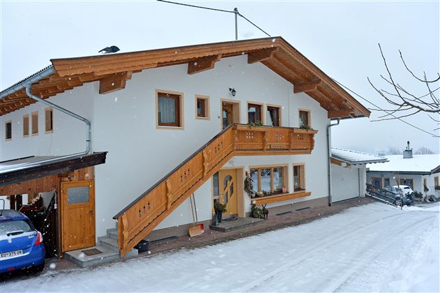 Ein gemütliches Haus im Schnee mit einem Holzbalcony. Die Umgebung ist winterlich und ruhig.