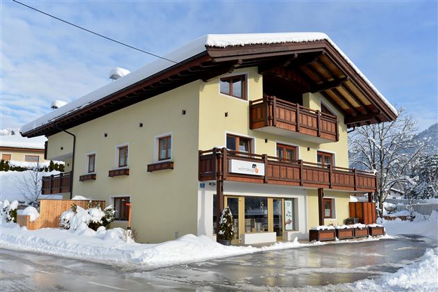 A beautiful building in the mountains, surrounded by snow. It has a traditional style with wooden balconies and a clear blue sky.