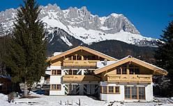 A beautiful chalet in the snow with impressive mountains in the background. The clear blue sky provides a picturesque alpine setting.