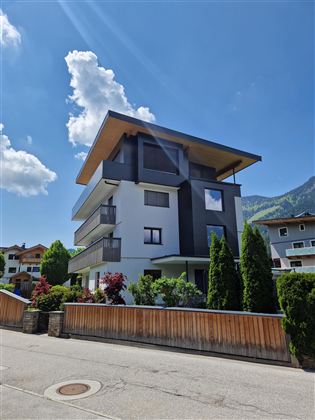 Ein modernes Gebäude mit mehreren Etagen und großen Fenstern. Umgeben von Bäumen und einer ruhigen Straße.