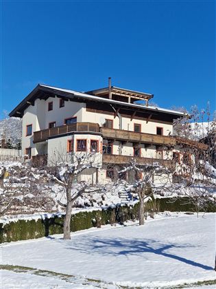 Ein modernes zweistöckiges Haus in einem verschneiten Landschaft. Im Hintergrund ist ein klarer blauer Himmel zu sehen.