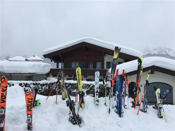 A chalet in the snow with many skis in front of the door. The sky is cloudy and the surroundings are wintry.