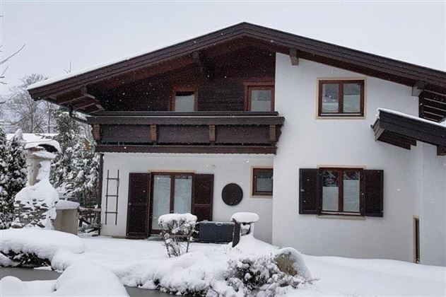 Ein weißes Haus im Schnee mit einem Dach in Holzoptik. Der Garten ist winterlich verschneit und ruhig.