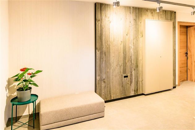 A modern entrance area with a padded stool and a plant on a table. The walls are in neutral tones, with wood paneling.