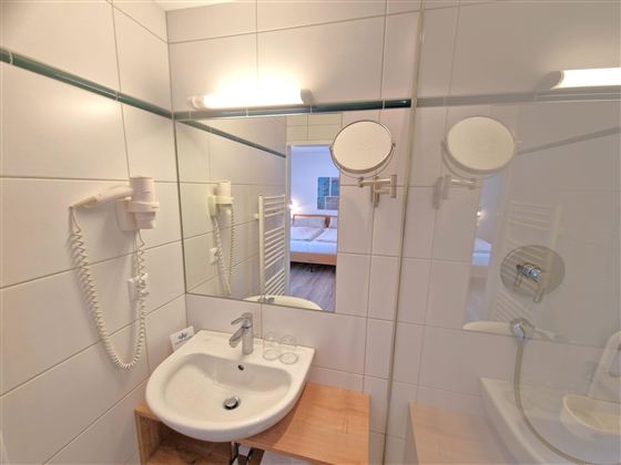 A modern bathroom with a sink and a large mirror. The walls are brightly tiled and there is a hairdryer.