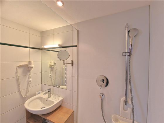 A modern bathroom with a shower and a sink. The walls are tiled with white tiles and there is a mirror.