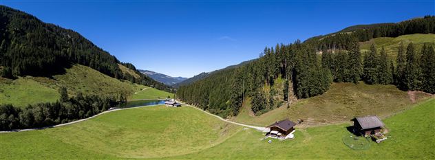 Eine weitläufige grüne Landschaft mit sanften Hügeln und Bäumen. Im Hintergrund sind kleine Hütten und ein klarer blauer Himmel zu sehen.
Chalet Heualm Kelchsau Kitzbüheler Alpen