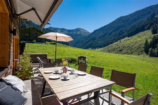 Ein schöner Außenbereich mit einem großen Esstisch und Sonnenschirm. Im Hintergrund sind grüne Berge und eine sonnige Landschaft zu sehen.
Chalet Heualm Kelchsau Kitzbüheler Alpen