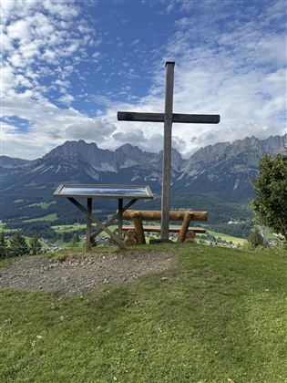 A view of the mountains with a wooden cross in the foreground. A bench-table combination invites you to linger.