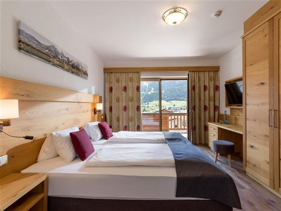 Doppelzimmer im Hotel Alpenpanorama in der Ferienregion Wilder Kaiser mit Holzmöbeln, gemütlicher Sitzecke und Ausblick ins Grüne.