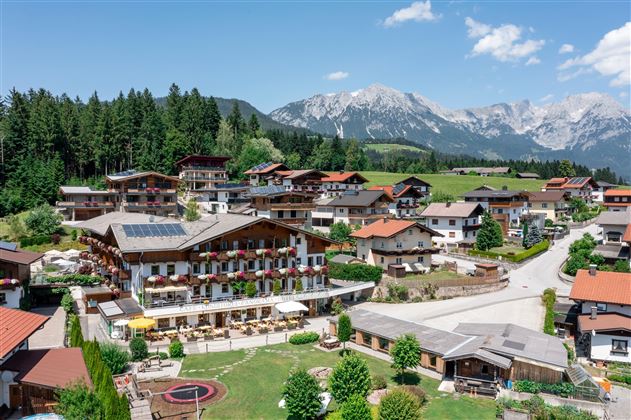 Luftaufnahme des Hotels Alpenpanorama mit umliegender Berglandschaft und Sonnenterrasse.