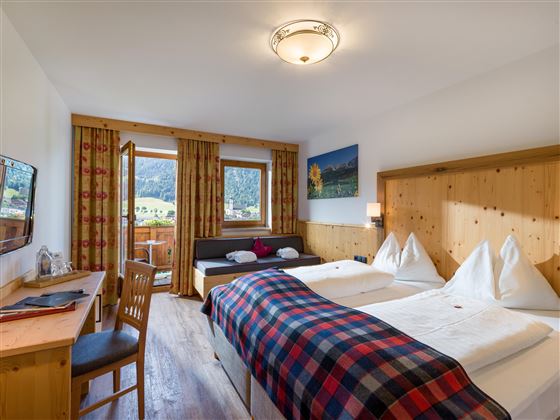 Gemütliches Doppelzimmer mit Holzmöbeln, karierten Details und Balkon mit Bergblick.