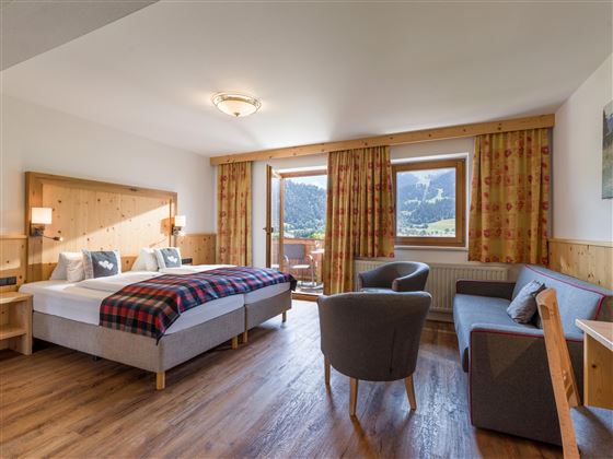 Großzügiges Doppelzimmer im Hotel Alpenpanorama in der Ferienregion Wilder Kaiser mit Sitzecke, Sofa, Schreibtisch und viel Tageslicht.