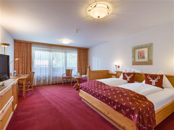 Komfortzimmer im Hotel Alpenpanorama in der Ferienregion Wilder Kaiser mit Boxspringbett, rotem Teppich und Balkonzugang.