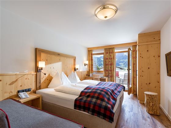 Gemütliches Doppelzimmer im Hotel Alpenpanorama in der Ferienregion Wilder Kaiser mit Holzbett, kariertem Plaid und Fensterblick in die Berge.