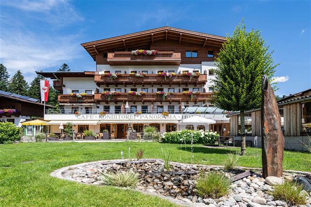 A charming guesthouse in a picturesque landscape with colorful flower boxes. The terrace invites you to relax outdoors, surrounded by green meadows and mountains in the background.