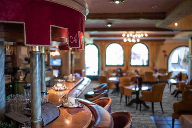 Eine gemütliche Innenansicht eines Restaurants mit einer Bar und Sitzplätzen. Die Fenster lassen natürliches Licht herein und schaffen eine einladende Atmosphäre.