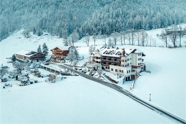 Eine winterliche Landschaft mit schneebedeckten Häusern und hohen Bäumen. Die Umgebung ist ruhig und verschneit, ideal für einen idyllischen Rückzugsort.