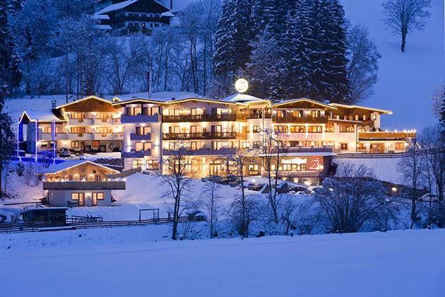 Ein gemütliches Hotel, das nachts im Schnee leuchtet. Umgeben von verschneiten Bäumen und einer winterlichen Landschaft.