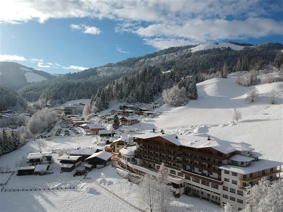 Eine winterliche Landschaft mit schneebedeckten Hügeln und einem kleinen Dorf. Die Gebäude sind in eine ruhige, weiße Decke aus Schnee eingebettet.