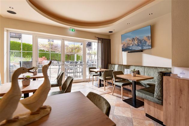 Ein gemütliches Café mit modernen Tischen und Stühlen. Große Fenster bieten einen Blick in den Außenbereich.