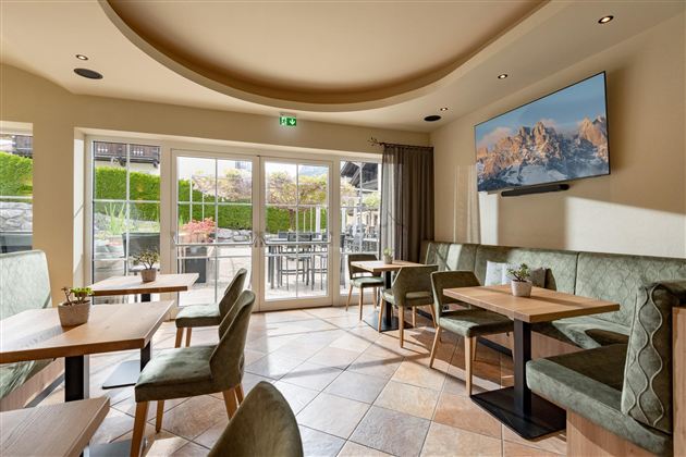 Ein einladendes Café mit modernen Tischen und Stühlen. Große Fenster und ein Fernseher zeigen eine schöne Berglandschaft.