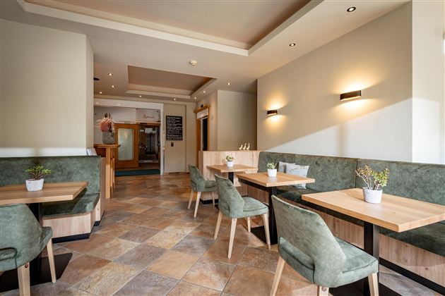 Ein modernes Restaurantinterieur mit Holz- und grünen Sitzen. Die Wände sind in neutralen Farben gehalten und es gibt gut beleuchtete Tafeln.