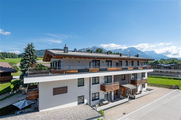 Ein modernes Gebäude mit Holzverkleidung in einer malerischen Landschaft. Im Hintergrund sind Berge und ein klarer blauer Himmel zu sehen.