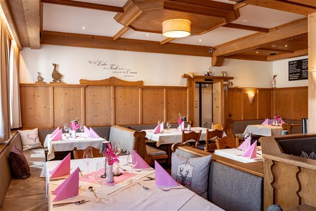 Ein gemütliches Restaurant mit Holzverkleidung und dekorativen Elementen. Die Tische sind hübsch gedeckt mit rosafarbenen Servietten und frischen Blumen.