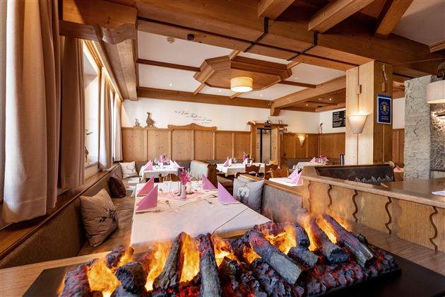 Ein gemütliches Restaurant mit Holzdekor und eleganter Tischdekoration. In der Mitte brennt ein stilvolles Feuer, das eine warme Atmosphäre schafft.