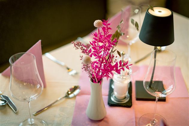 Ein stilvoll gedeckter Tisch mit einer pinken Blumenvase und eleganten Gläsern. Die Atmosphäre wird durch eine kleine Lampe und dekorative Elemente unterstrichen.