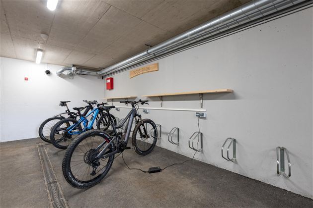 Ein moderner Fahrradabstellraum mit mehreren E-Bikes und Ladeanschlüssen. Die Wände sind schlicht und abweisend, was einen sauberen Eindruck hinterlässt.