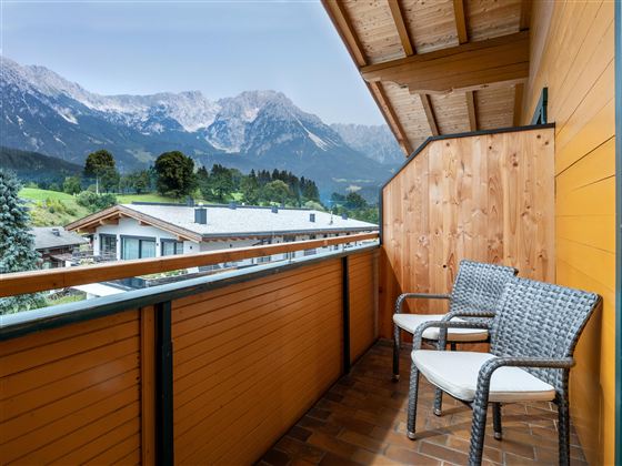 Ein gemütlicher Balkon mit zwei Stühlen und Blick auf die Berge. Die Umgebung ist ruhige und naturbelassene.