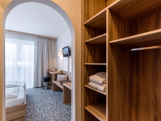 Ein modernes Zimmer mit einem gemütlichen Bett und einem Arbeitsbereich. Die Fenster lassen viel Licht herein und die Holzregale bieten Stauraum.