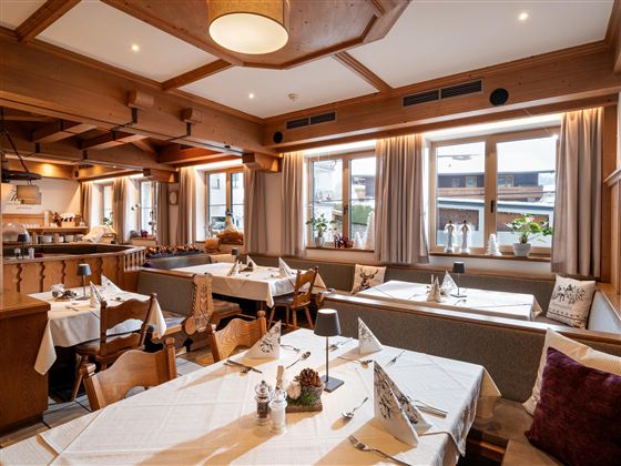 Ein gemütliches Restaurant mit Holzdekor und Tischdecken. Die Fenster lassen viel Licht herein und bieten einen Blick nach draußen.