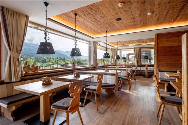 Een modern restaurant met houten meubels en grote vensters die uitzicht op de bergen bieden. De inrichting is gezellig en uitnodigend.