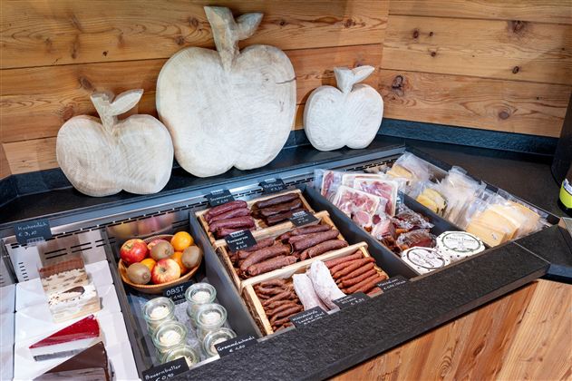 Een selectie van vleeswaren en snacks ligt op een houten plank. Op de achtergrond zijn decoratieve houten appels te zien.