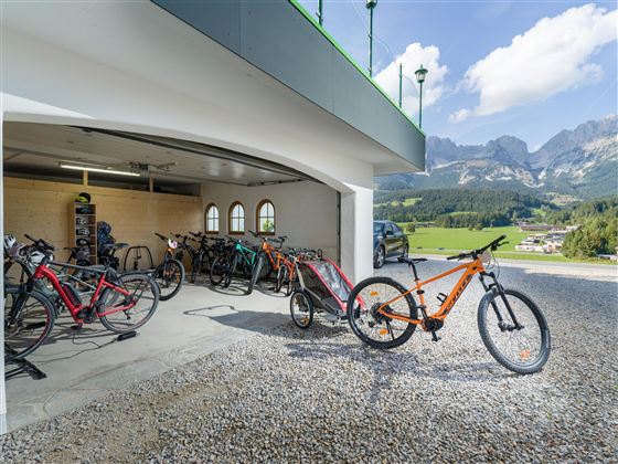 A garage with several bicycles and a beautiful mountain view. The surroundings are sunny and inviting.