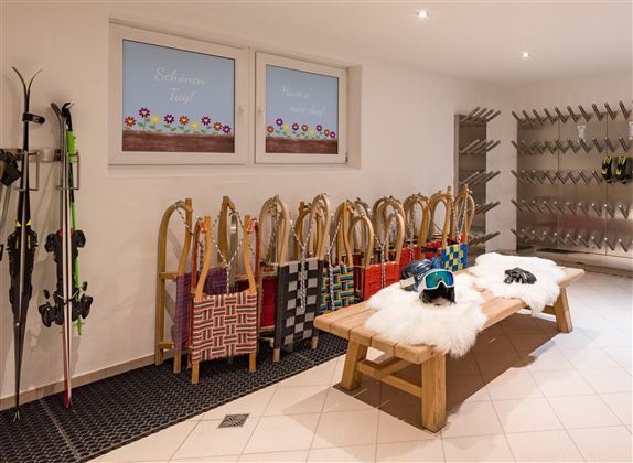 A cozy room with ski equipment and colorful bags. A wooden bench with a fur and a ski goggle are clearly visible.