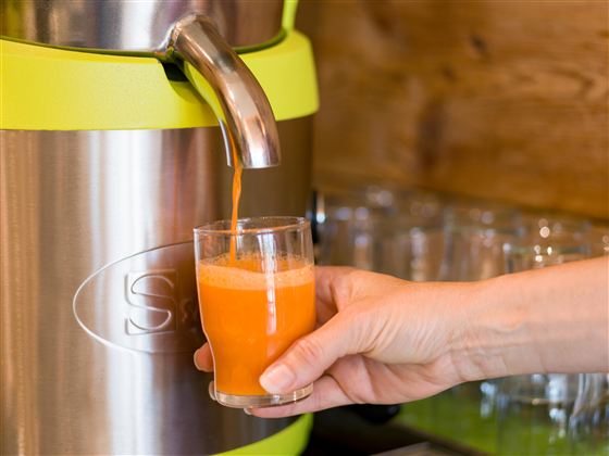 Een drankdispenser met verse, oranje sap wordt in een glas gegoten. Een hand houdt het glas vast terwijl het sap wordt ingeschonken.
