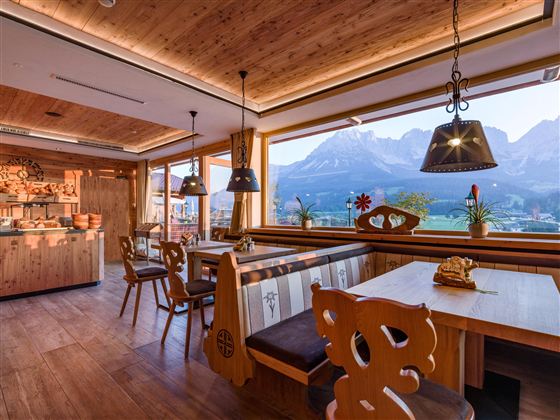 Een gezellig restaurant met houten interieur en grote ramen. Op de achtergrond zijn indrukwekkende berglandschappen te zien.