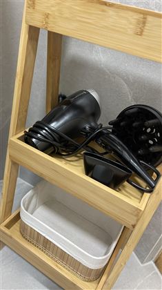 Een houten plank met een zwarte haardroger en een kom. Onder de plank bevindt zich een mand.