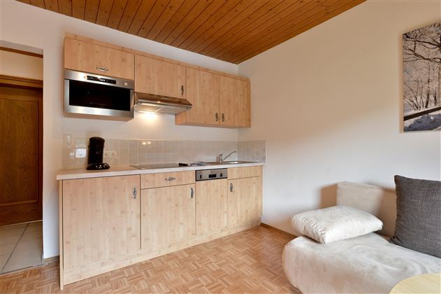 Eine moderne Küchenzeile mit Holzschränken und einem Herd. Daneben befindet sich ein gemütliches Sofa in einem hellen Raum.