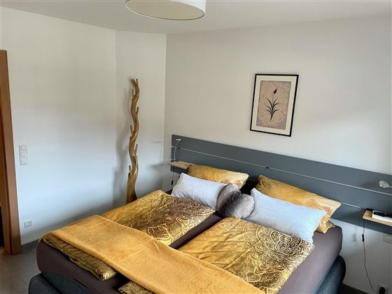 Ein gemütliches Schlafzimmer mit einem großen Doppelbett und gelben Bettdecken. An der Wand hängt ein dekoratives Bild, und eine Holzskulptur steht im Raum.