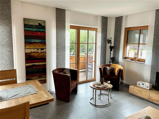 Ein modernes Wohnzimmer mit zwei gemütlichen Sesseln und einem Tisch. Große Fenster lassen viel Licht herein und bieten einen Blick auf den Außenbereich.