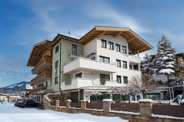 Ein modernes Gebäude im alpinen Stil, umgeben von Schnee und einem klaren Himmel. Im Vordergrund ist eine ruhige Straße mit einigen Fahrzeugen zu sehen.