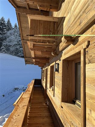 A wooden house with a balcony, surrounded by snow-covered landscapes. The architecture is traditional and cozy.