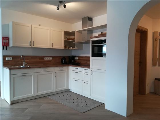 A modern kitchen with white cabinets and wooden details. It is well-equipped and has plenty of natural light.